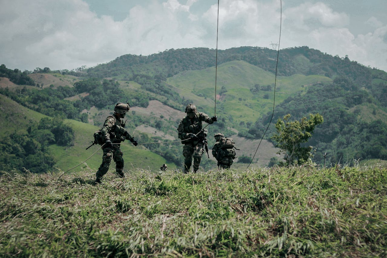 Three soldiers in military gear navigate grassy hills in Colombia during a tactical exercise.
